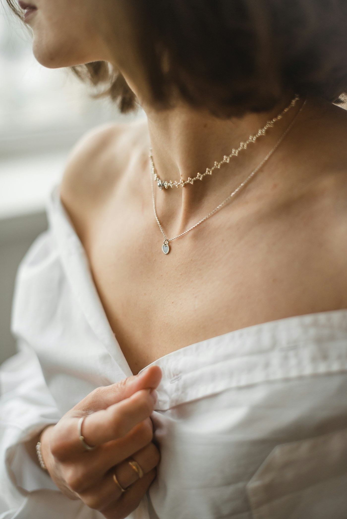 Delicate gold-tone earrings and a simple chain laid beside a white shirt